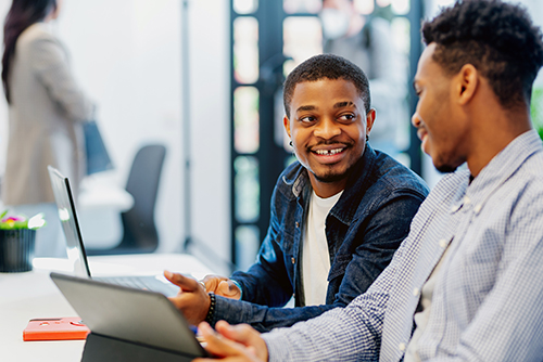 two men smiling and chatting at a desk