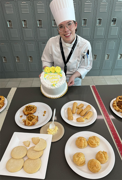 Ainsley Roberts in chef hat showing off cake.