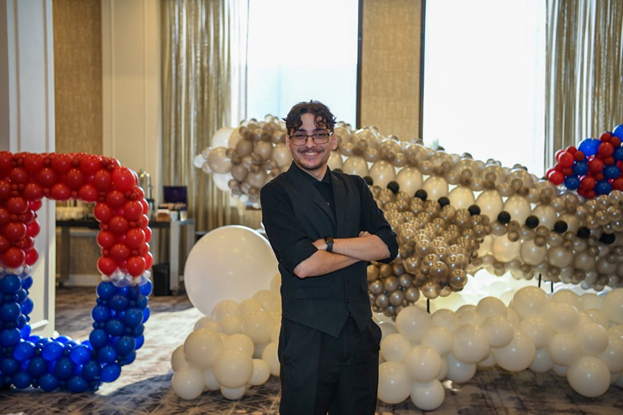 Andrew Prichard standing in front of balloon sculpture of airplane and big D at Student Leadership Conference.
