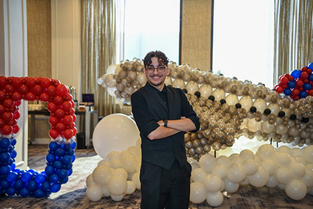 Andrew Prichard standing in front of balloon sculpture of airplane and big D at Student Leadership Conference.