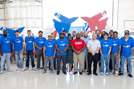 A group of students in the aviation maintenance technology program stand in front of cardboard airplanes at a ribbon-cutting event
