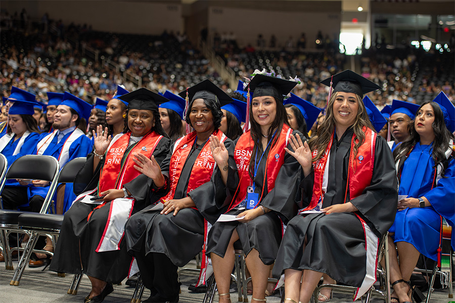A group of nursing students sit at graduation in their caps and gowns.