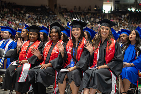 A group of nursing students sit at graduation in their caps and gowns.