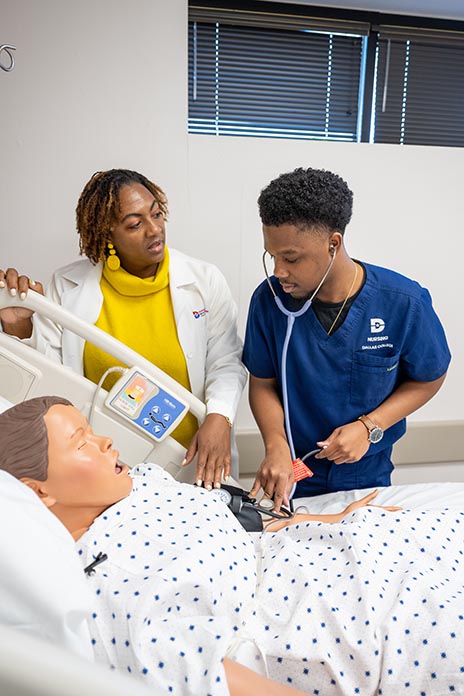 Student and instructor using stethoscope on manikin.