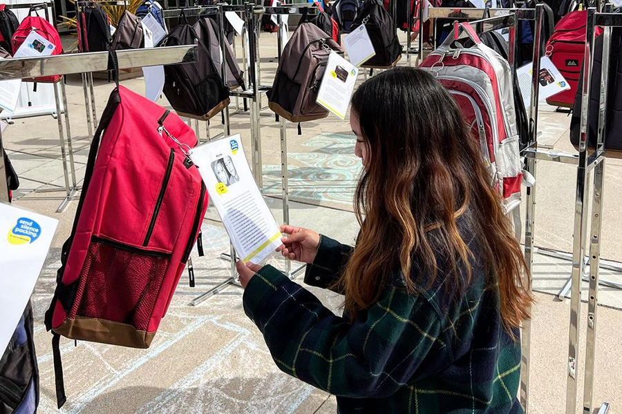 A student stands in front of a backpack reading a story as part of the Send Silence Packing exhibit.