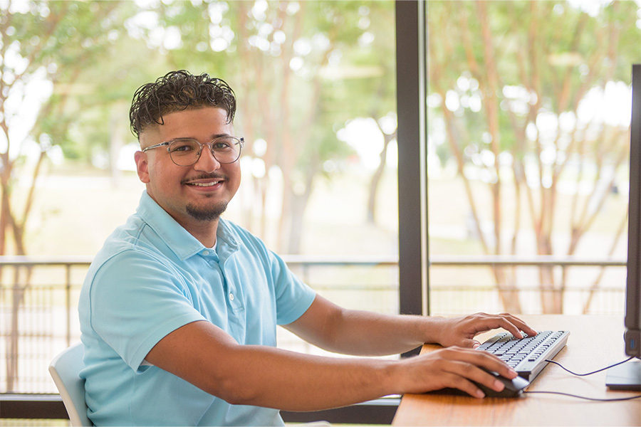 Cristian Castillo sits at a computer with his hands on the keyboard, looking at the camera.