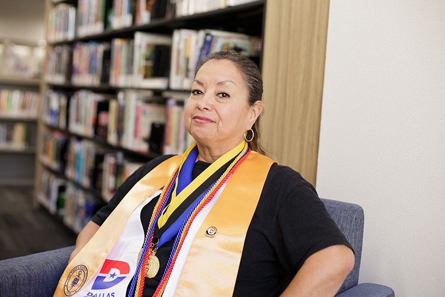 Marisol Perez sits in the library wearing her graduation regalia.