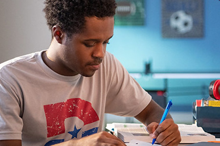 A student sits at the desk in their bedroom and studies