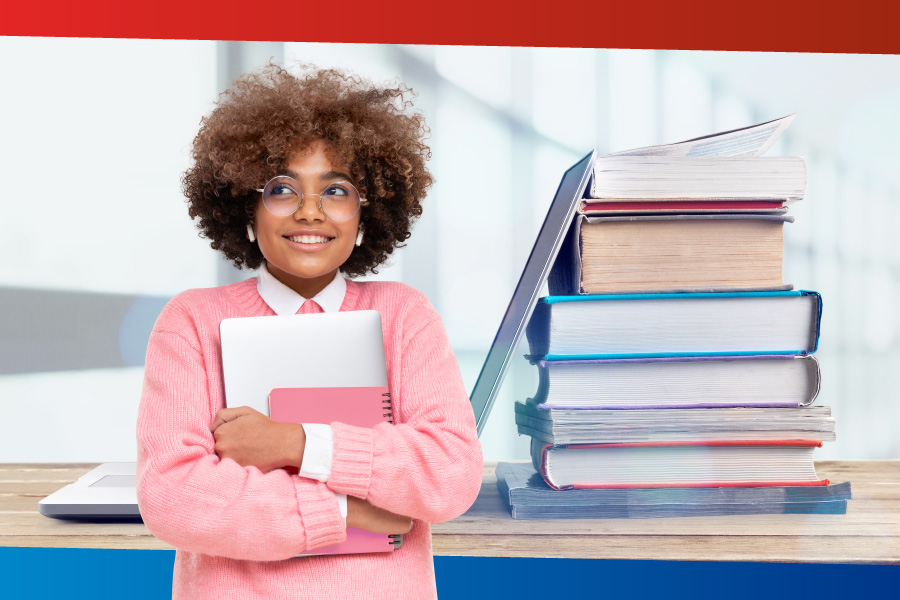 A student stands holding a notebook with books in the background.