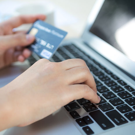 Close-up of hands holding a credit card while typing on a laptop keyboard