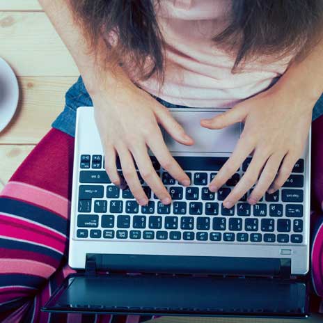 Person sitting cross-legged and typing on a laptop, filling out a loan application online