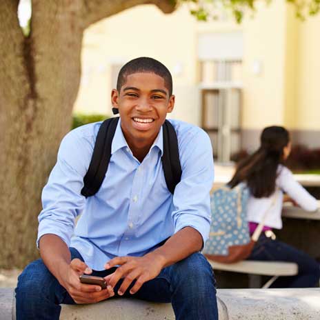 Smiling student with backpack using smartphone on college campus