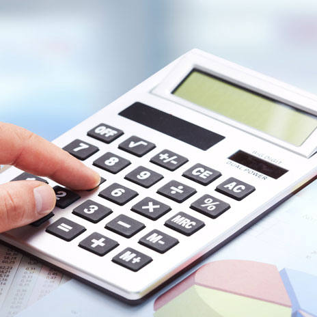 Close-up of a hand on a calculator, with blurred documents in the background.