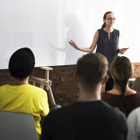 Teacher presenting to a seated students in a classroom setting