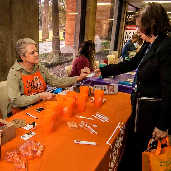 Representative at a career fair booth handing materials to an attendee, with promotional items