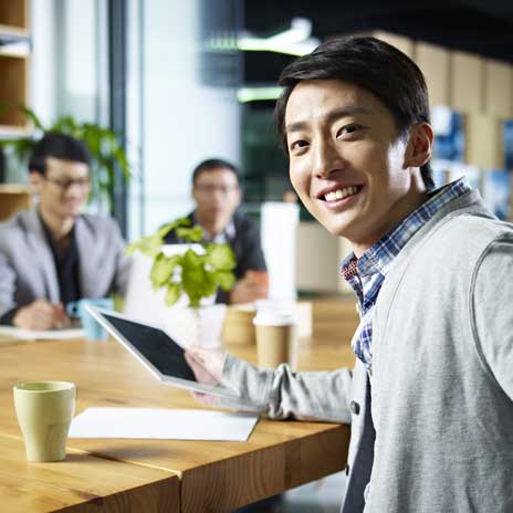 Person smiling while holding a tablet at a collaborative office table with colleagues