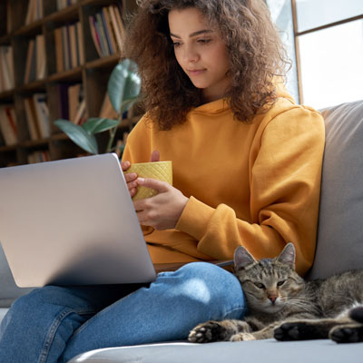 A student viewing a laptop screen on a sofa with a cat.