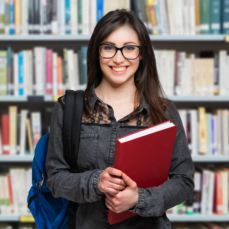 Student holding a red book in front of bookshelves in a library
