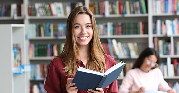 Students reading a book in a library with shelves in the background.