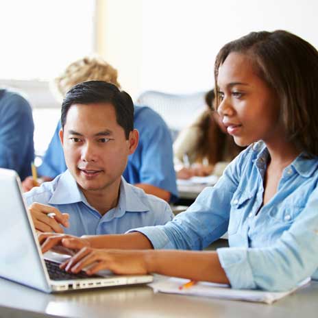 Two people working together on a laptop in a classroom