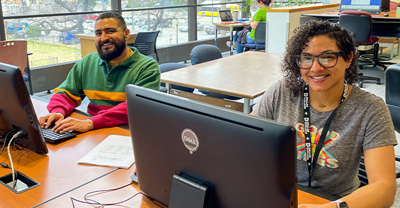 Two students sit behind computer monitors in the computer lab