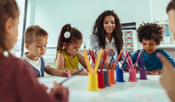 Group of kids oloring with a teacher at a table