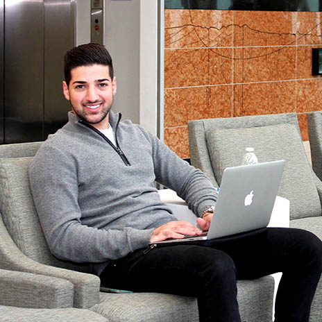 a friendly student success coach sitting on a chair with a laptop smiling