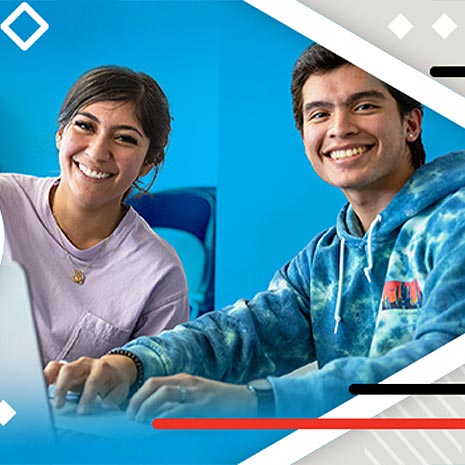 two students sitting and smiling at a desk working together