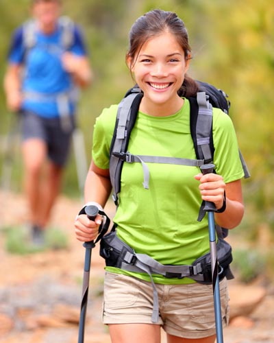 A woman wears a backpack and uses a walking stick while hiking