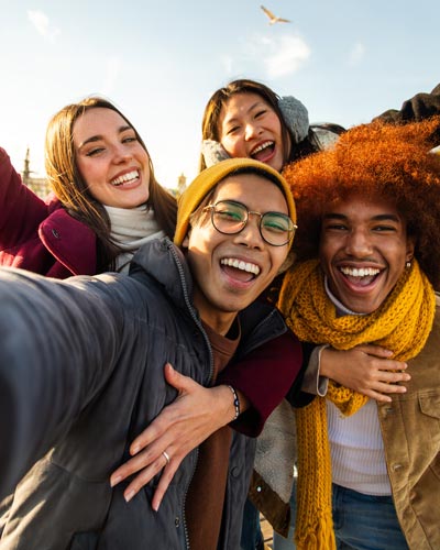 A group of friends laugh as they lean into the camera with their arms wrapped around one another
