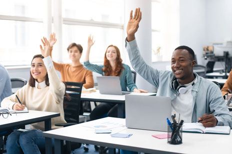 classroom with students sitting at desks raising hands