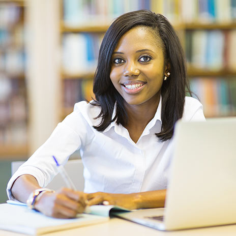 female student sitting at laptop with a notebook and smiling