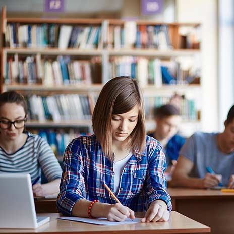 female studying at a desk with laptop paper and pencil