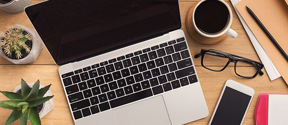 A laptop, notes and office supplies sit on a desk