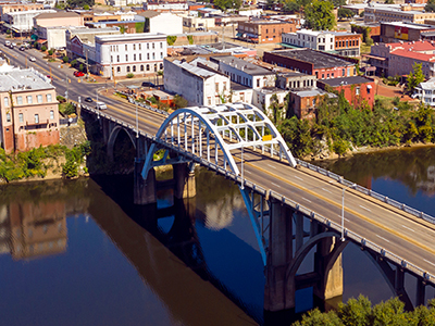 Aerial view of an arched bridge over a calm river, leading into a historic town