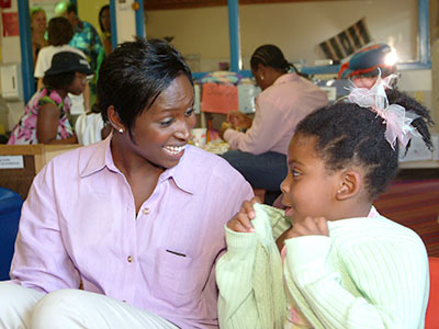 A woman in a pink shirt smiling at a young girl in a green sweater