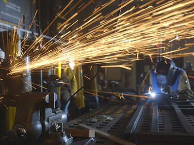 A worker welds metal on a table, emitting bright sparks and creating a dynamic scene