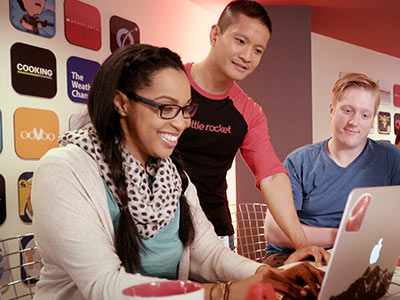 Three people collaborate happily around a laptop in a modern office
