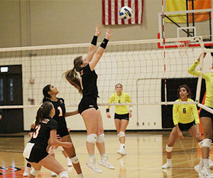 A Cedar Valley Volleyball player jumps to block a ball coming over the net