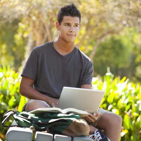 A student sits outside with an open laptop in his lap