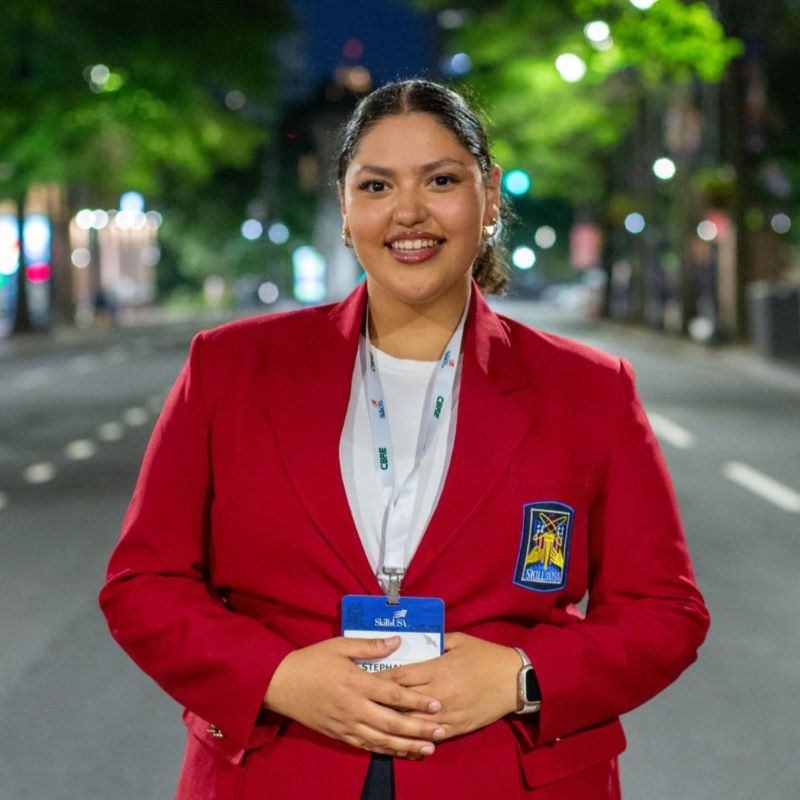 A student with a red jacket poses for a photo in a downtown setting