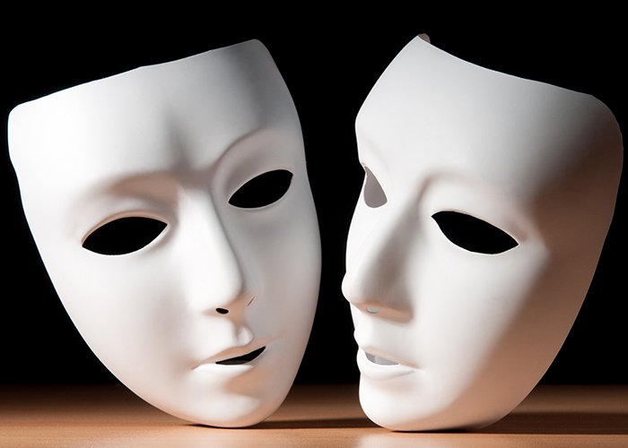 Two white theater masks on a table with a black background behind them