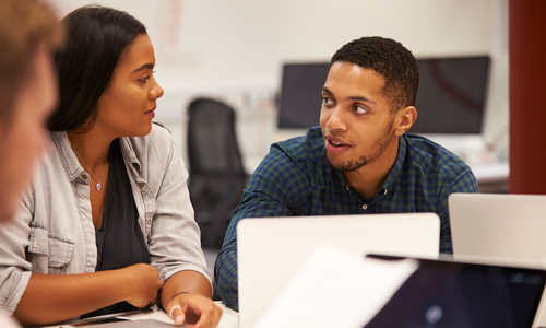 Students talk while sitting at desk in a computer lab