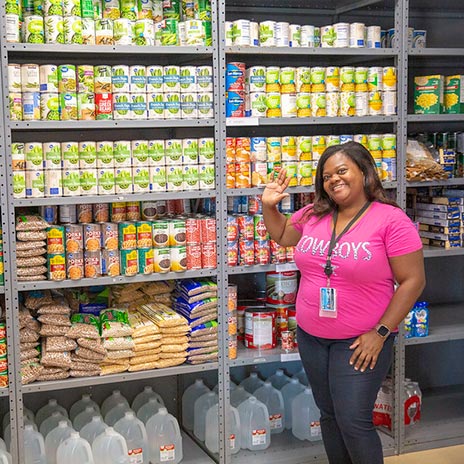 a volunteer stands in front of shelves filled with food at a Dallas College food pantry