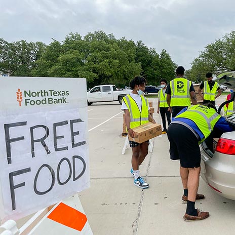 volunteers load food into a car trunk next to a sign that says 