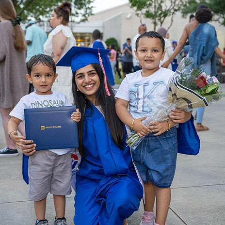 a woman graduate wearing cap and gown poses with two young children