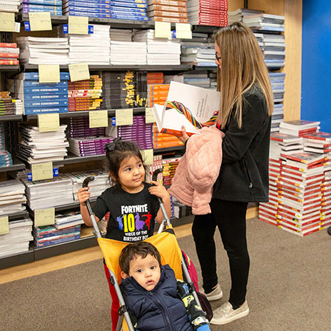 a woman flips through a textbook in a college bookstore while her two young children wait