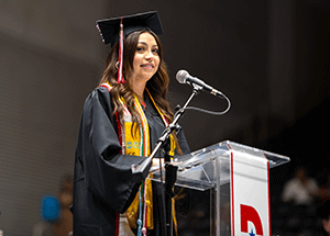 Erika Ramirez stands at a lectern in her graduation cap and gown.