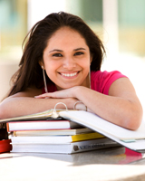 Student smiling with hands resting on stack of textbooks