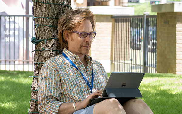 A student sits outside El Centro Campus working on a tablet